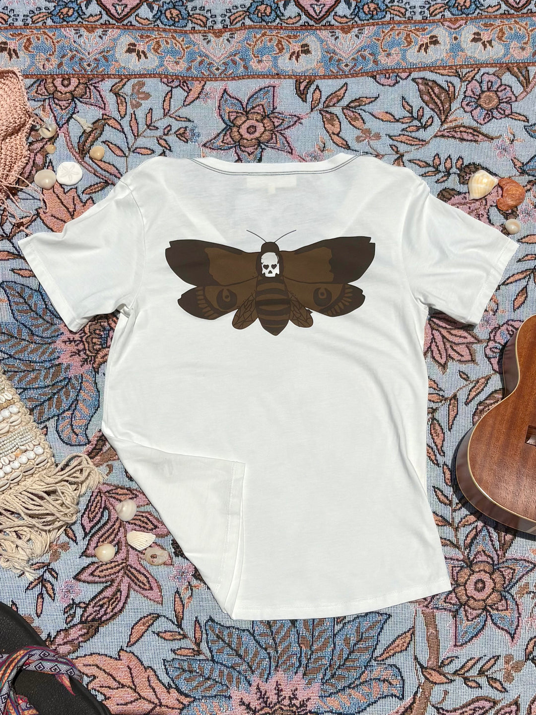 white v-neck tee with brown skull/moth depiction on back.