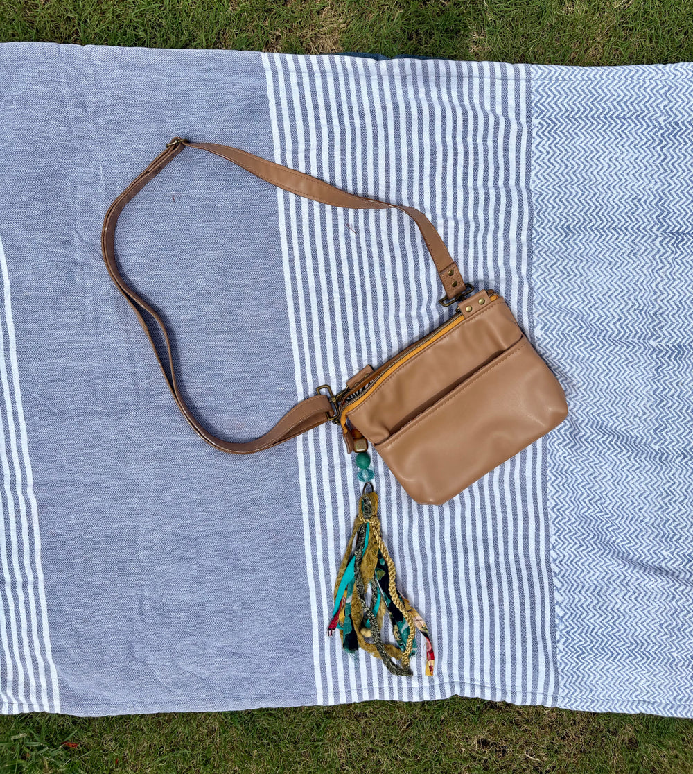 small, tan crossbody with blue/green fringe clip-on accessory.