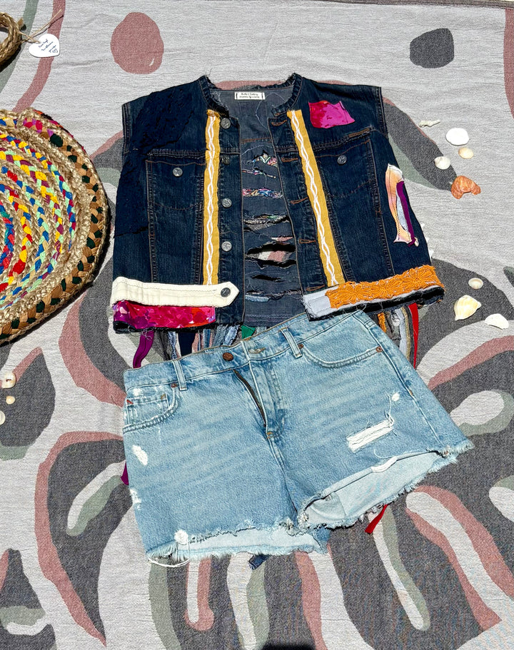cropped, dark denim vest with colorful patchwork and long fringe off the back.